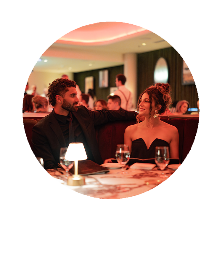 Valentine's Day Text below a circular image of a couple sitting at a table with glasses at a restaurant