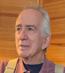 Close-up of Walter Alexander, wearing a colorful shirt, standing in front of a wooden wall.