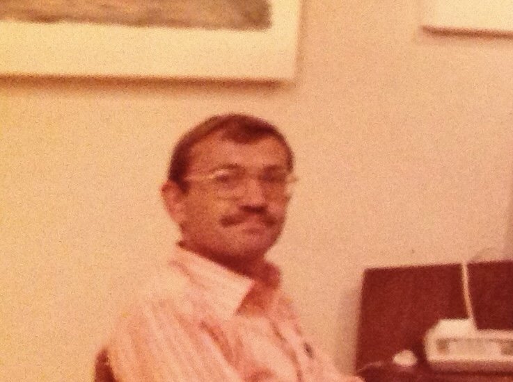 Close-up of Ted Petrenko, with glasses and a mustache sitting in an indoor setting, wearing a light-colored, striped shirt.