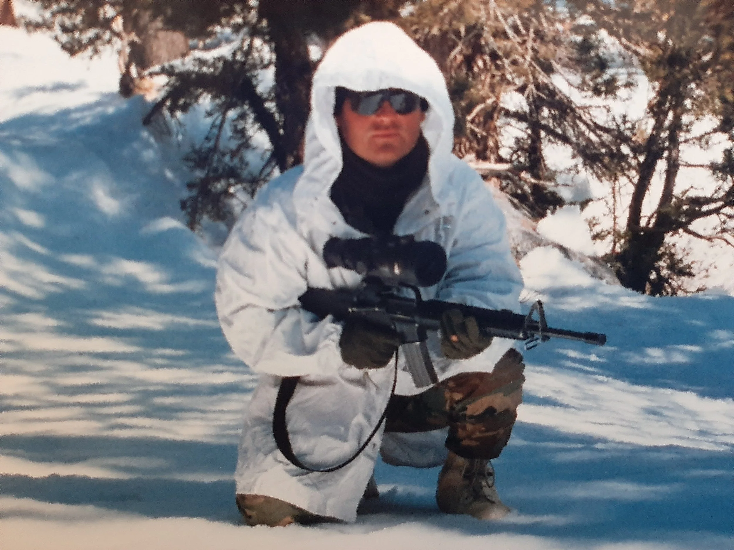 Soldier dressed in white crouched in snow holding a rifle