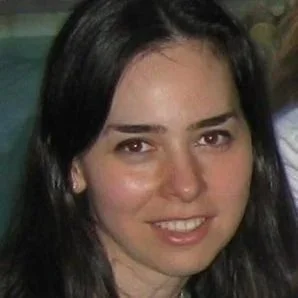 Headshot of a woman with long dark hair, smiling against a softly blurred background.