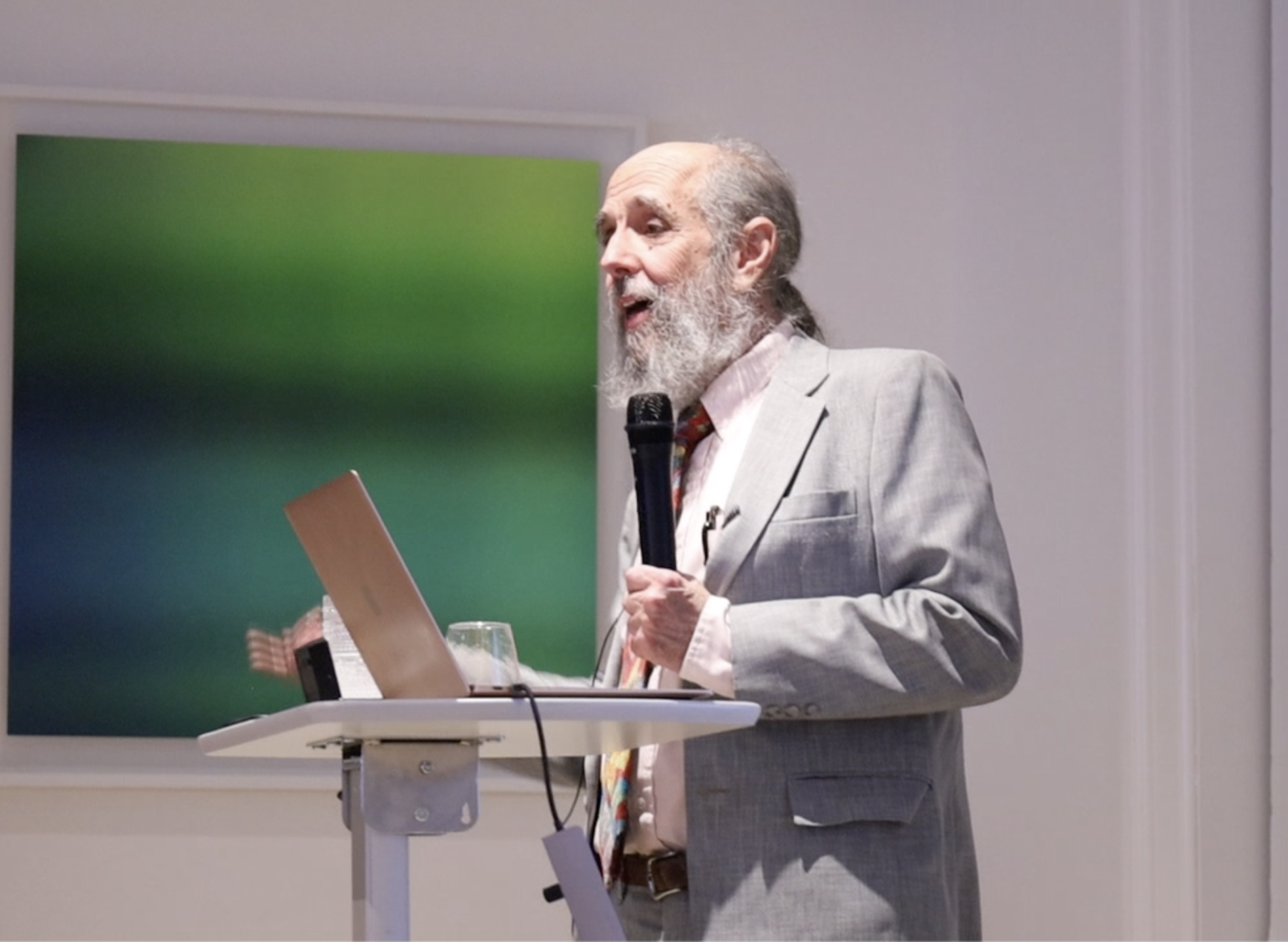 Older gentleman presents on a topic in front of a podium with a microphone