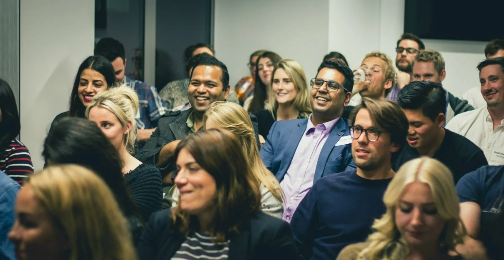 Group of people attending a conference or seminar, sitting in chairs, smiling, and enjoying the presentation.