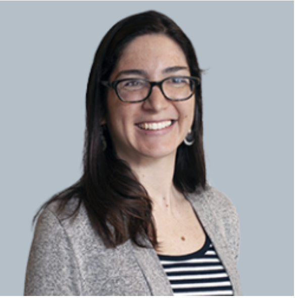 A woman with long blonde hair smiling, wearing a black and white blouse with lace details.
