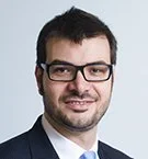 A woman with long blonde hair smiling, wearing a black and white blouse with lace details.