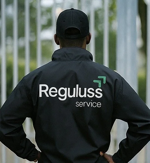 Mann trägt schwarze Jacke mit dem Logo und Schriftzug 'Reguluss service' auf dem Rücken, steht vor einem Gitterzaun.