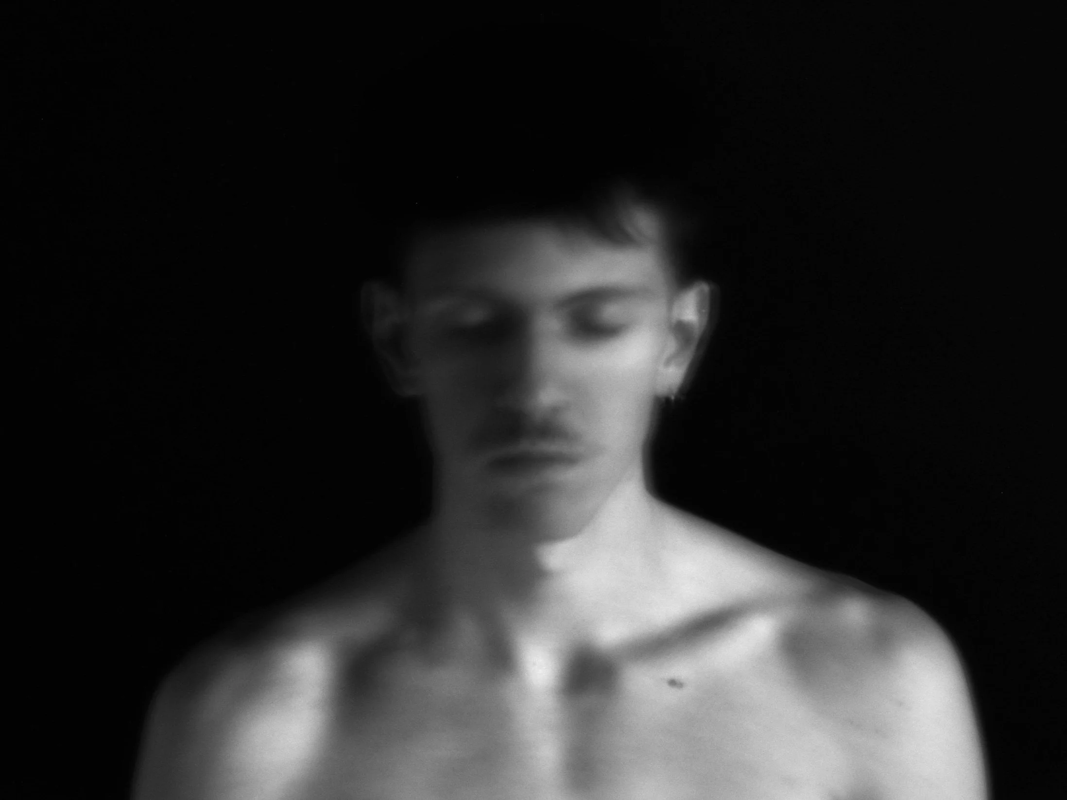 Verschwommene Aufnahme eines Oberkörpers und Gesichts, vor schwarzem Hintergrund, s/w.