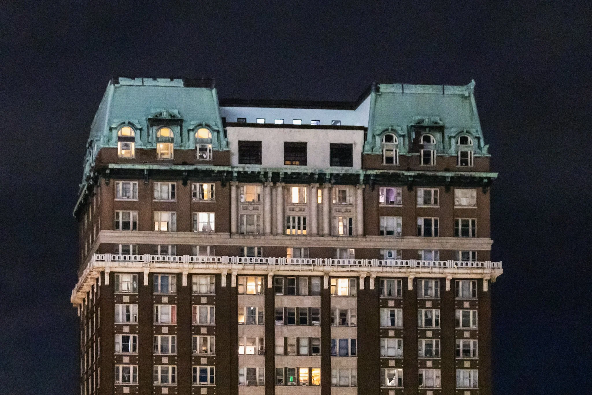 Nighttime photo of the upper stories of The Exchange Building in Memphis, Tennessee, showing its illuminated windows, dark brick façade, and distinctive green-patinated mansard roof set against a black sky.