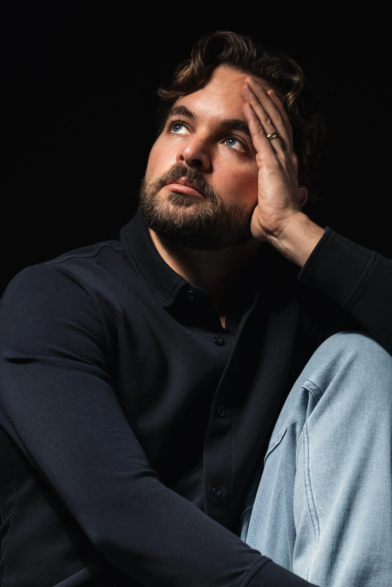 Portrait of Matt Rutter, Cleveland-based award-winning photographer specializing in pet portraits, real estate photography, and UGC content, captured in dramatic chiaroscuro studio lighting against a black background. He gazes upward thoughtfully wit