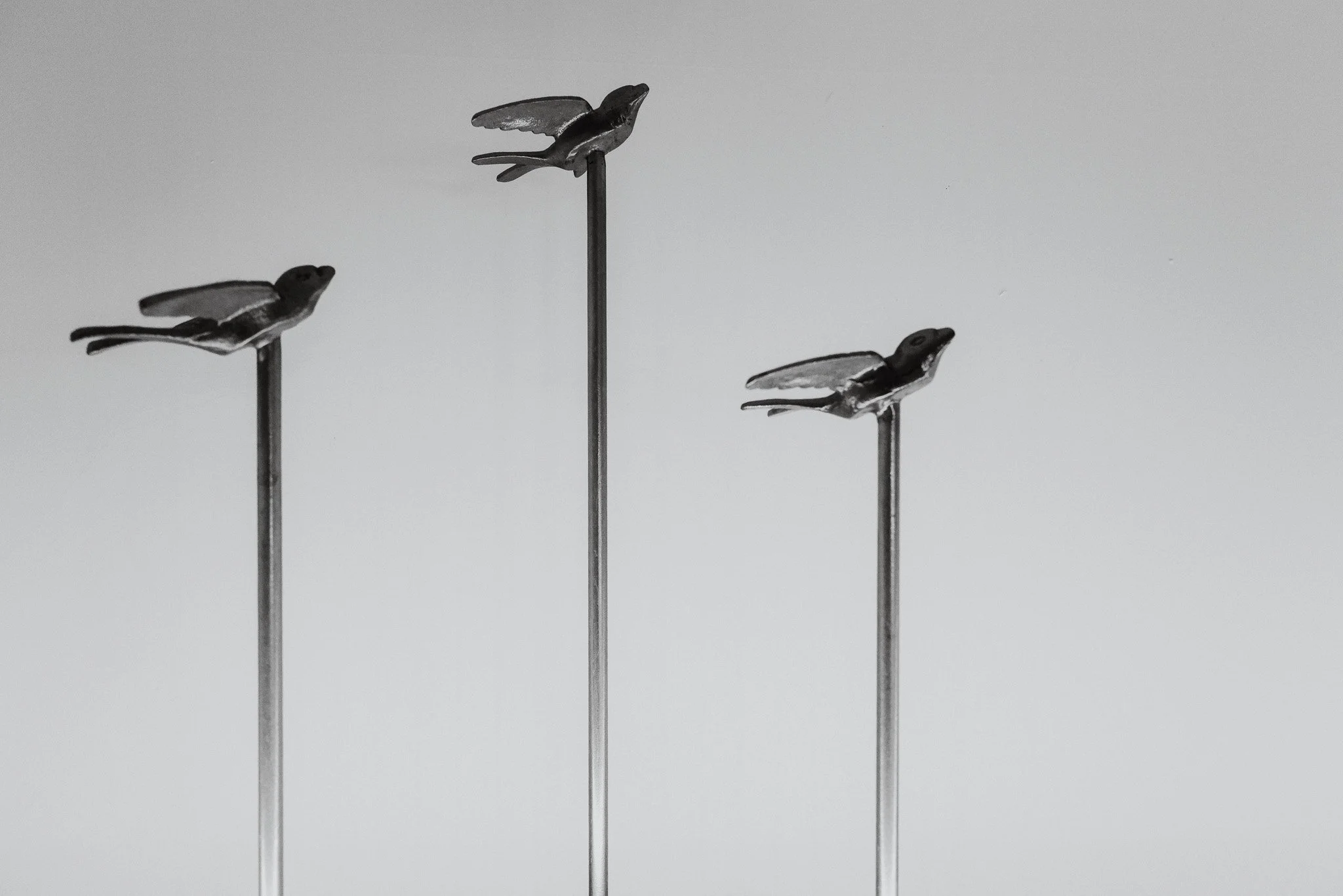 Three metallic bird sculptures mounted on thin rods against a plain background.