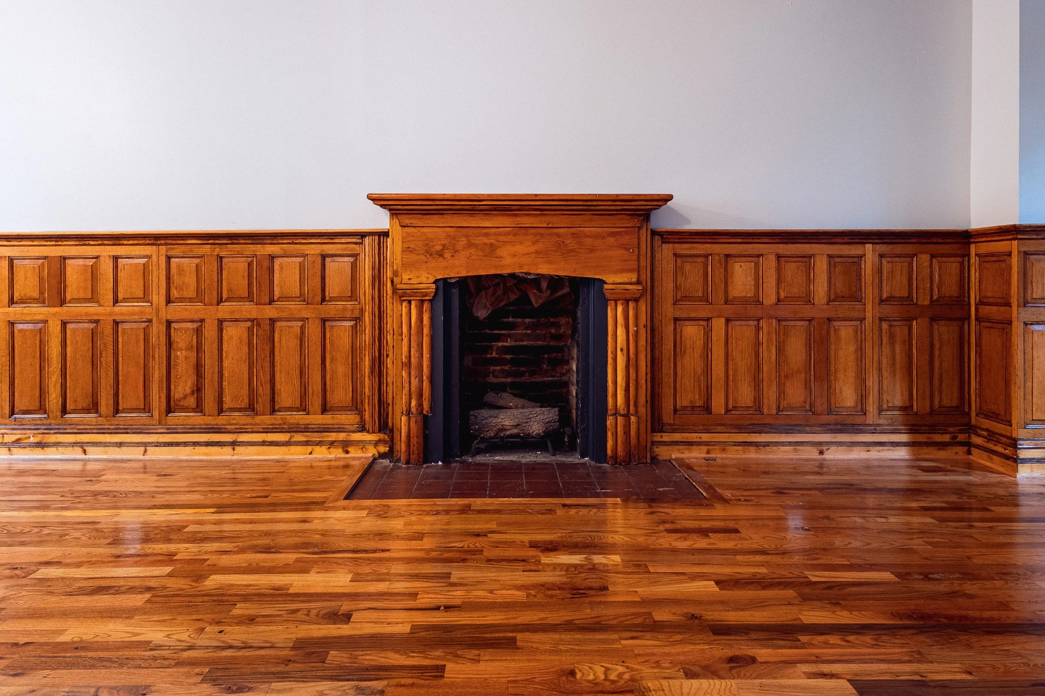 Wood-paneled wall with fireplace, empty hearth, and hardwood floor.