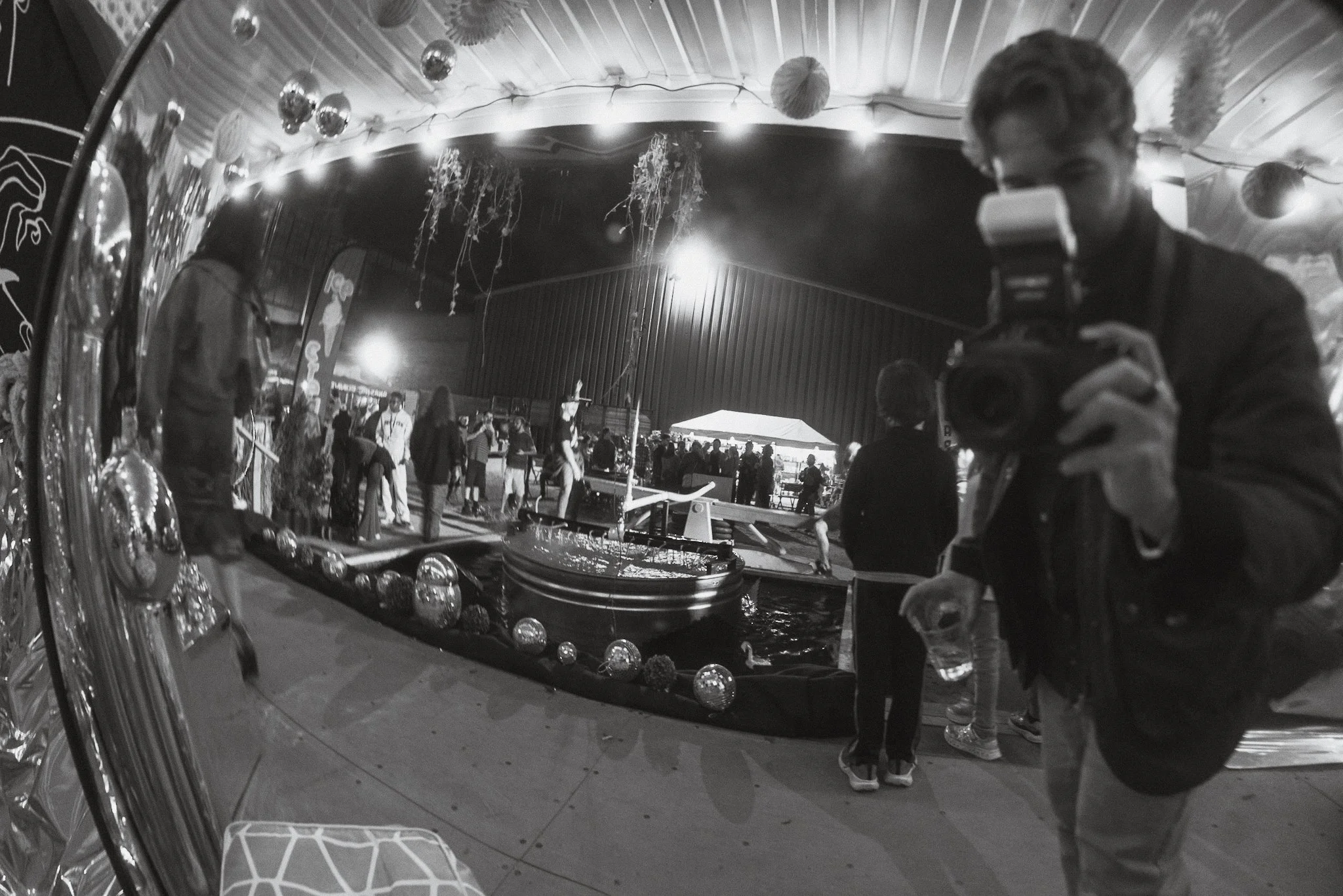 Reflection in a decorative mirror shows a woman taking a photo at a festive event with balloons and people in the background.