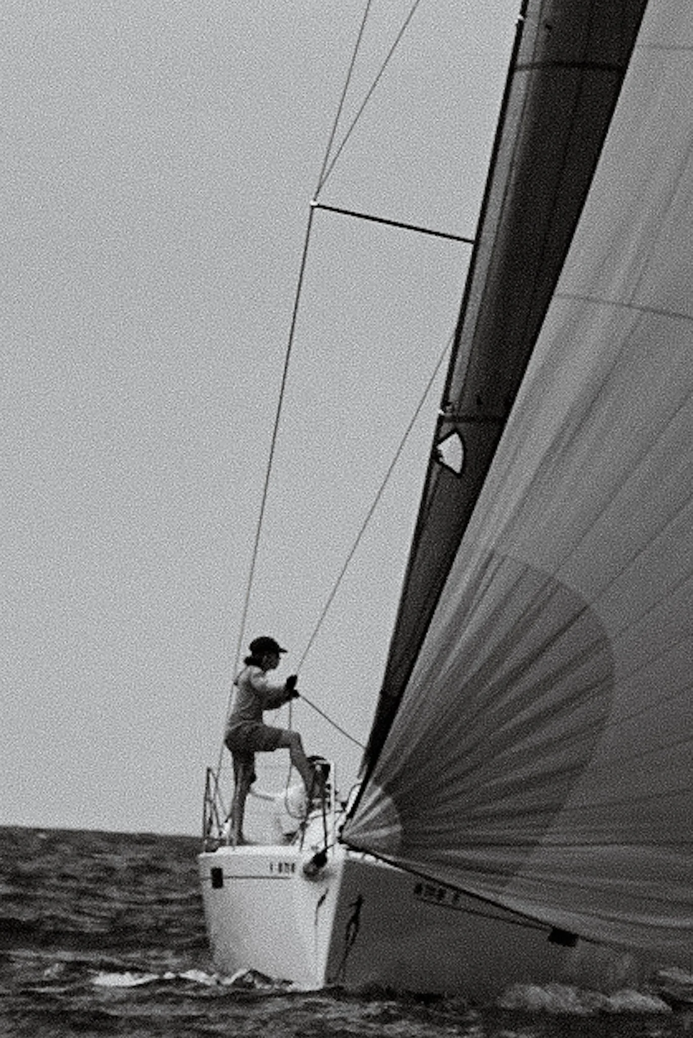A person standing on a boat, inspecting or working on the side of a large yacht or ship, with water below and cable or wire overhead.