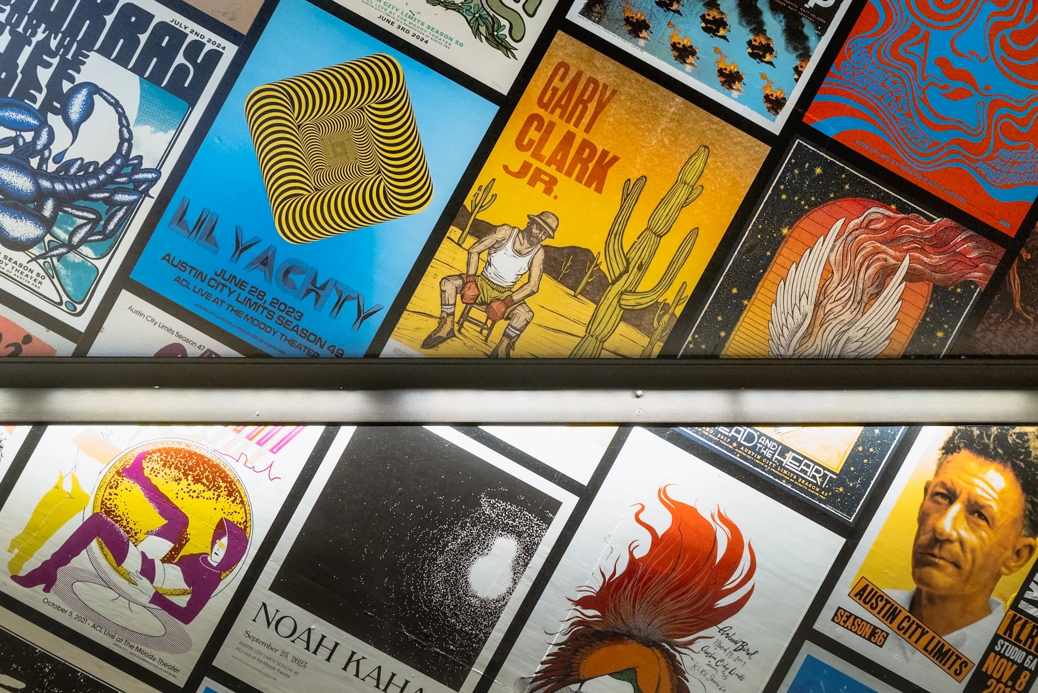 A collage of various colorful event posters, including a poster with a black scorpion on a white background, a poster with yellow and black hypnotic spirals, a poster with a cowboy and cacti titled "Gary Clark Jr." with a yellow background, and other