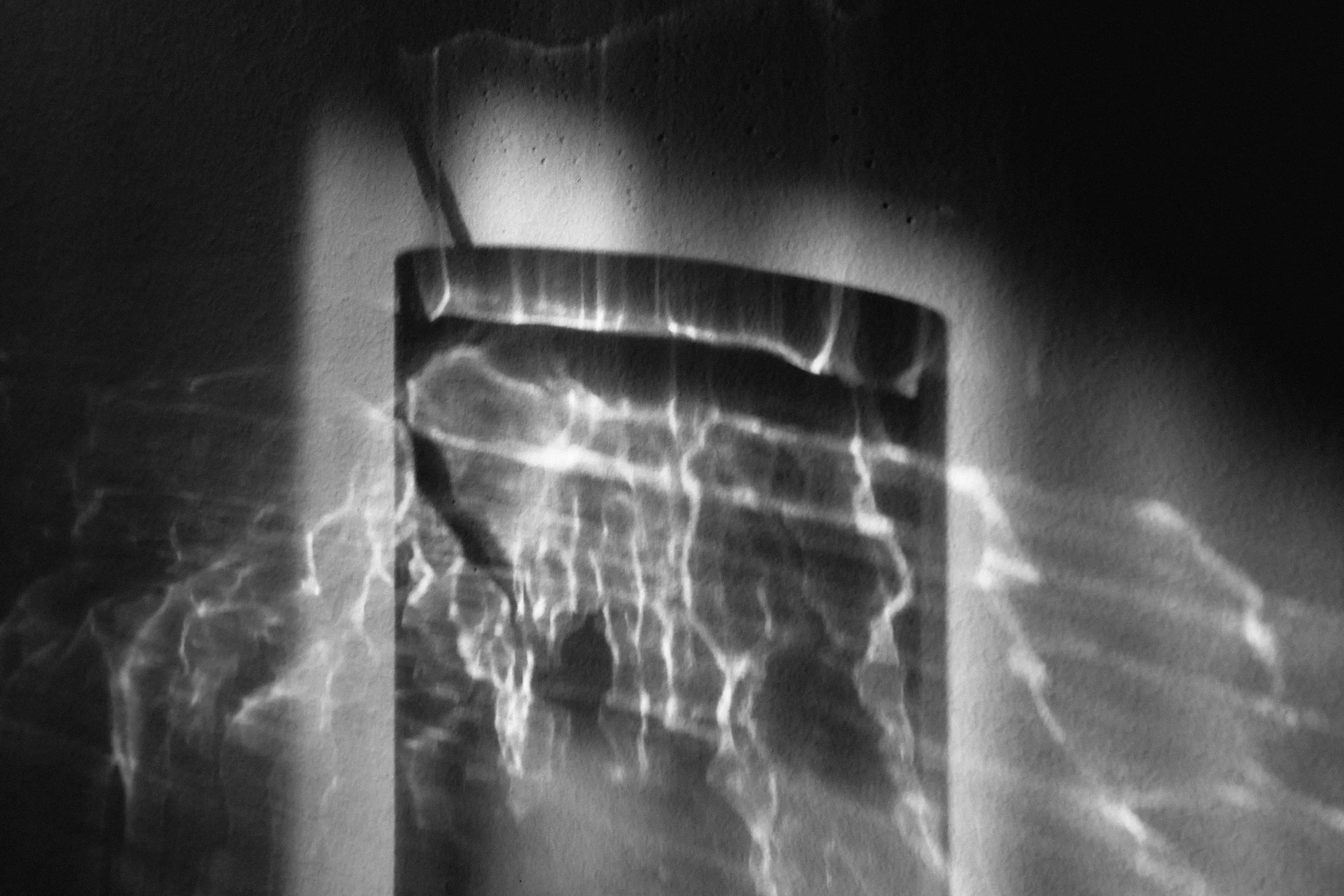 A black and white photo of a chair with a shadow cast by a glass of water filled with water on a table.