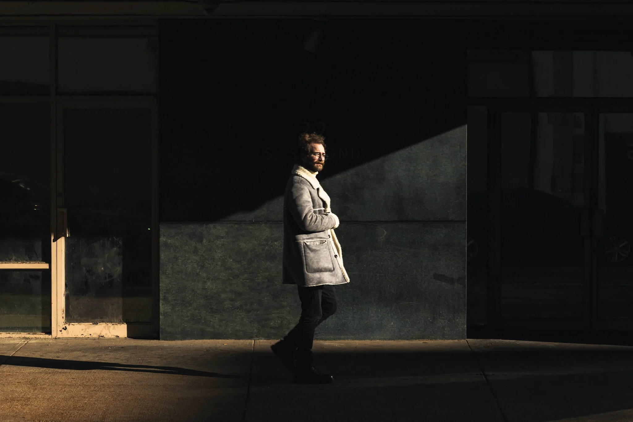 Street photography scene in downtown Memphis with strong contrast from late afternoon light casting long shadows across the sidewalk. A single person walks through the light after the photographer waited several minutes for the right moment.