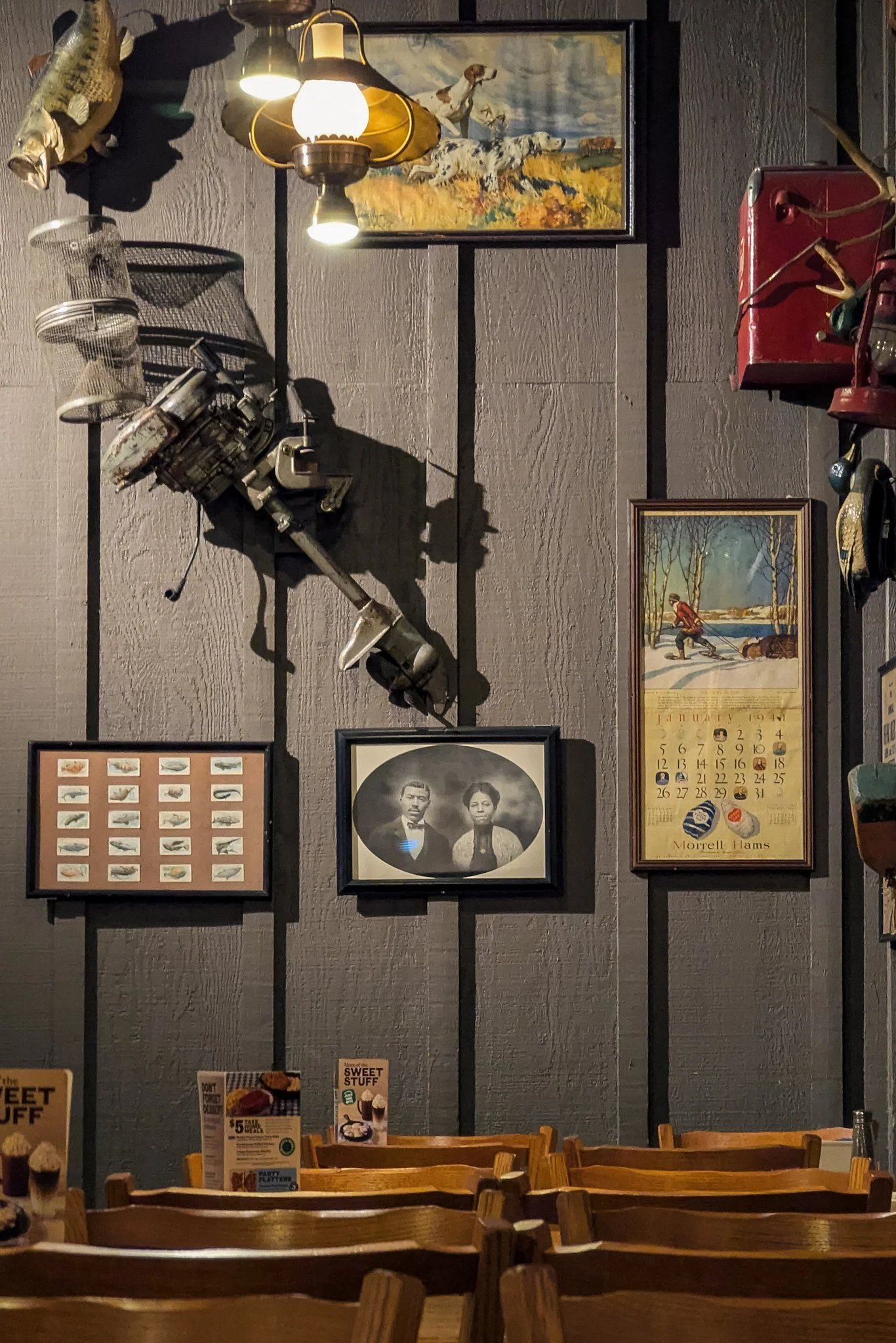 Rustic Cracker Barrel wall with warm-glowing brass lamps, a painting of a pointer dog in golden fields, vintage sepia portraits of suited men, an old movie camera casting long shadows, a winter hunt scene print, a red fire extinguisher, a bird displa