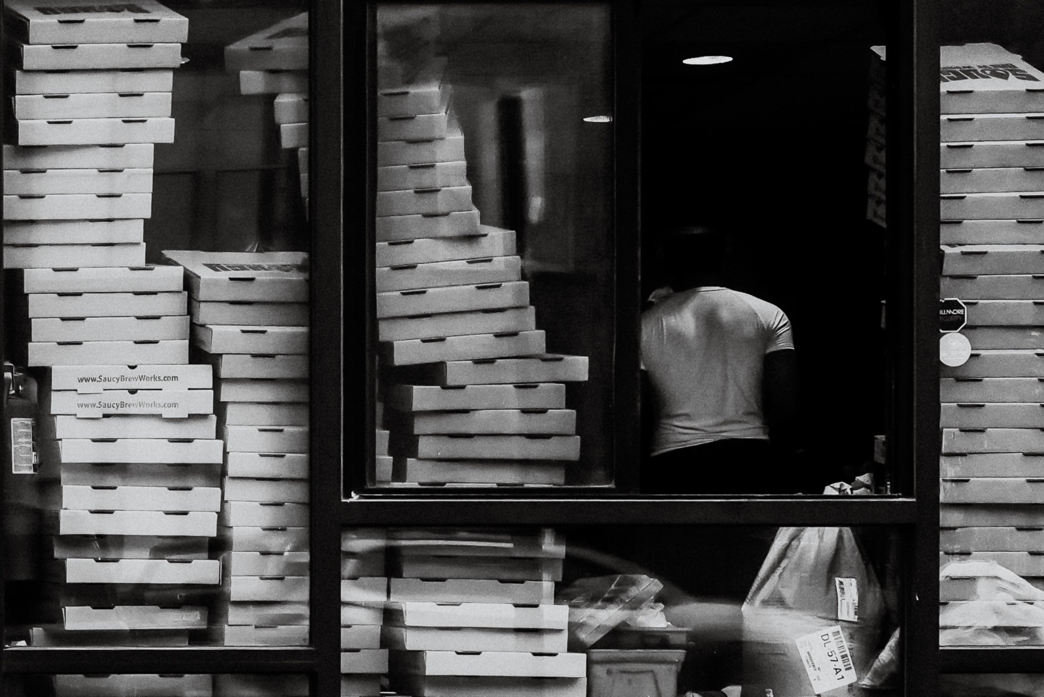 Stacks of pizza boxes on shelves with a person partially visible behind them.