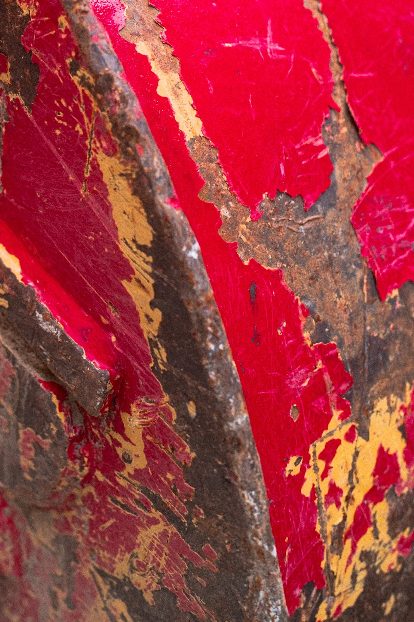 Close-up of a weathered metal surface with peeling red and yellow paint, revealing rust underneath.