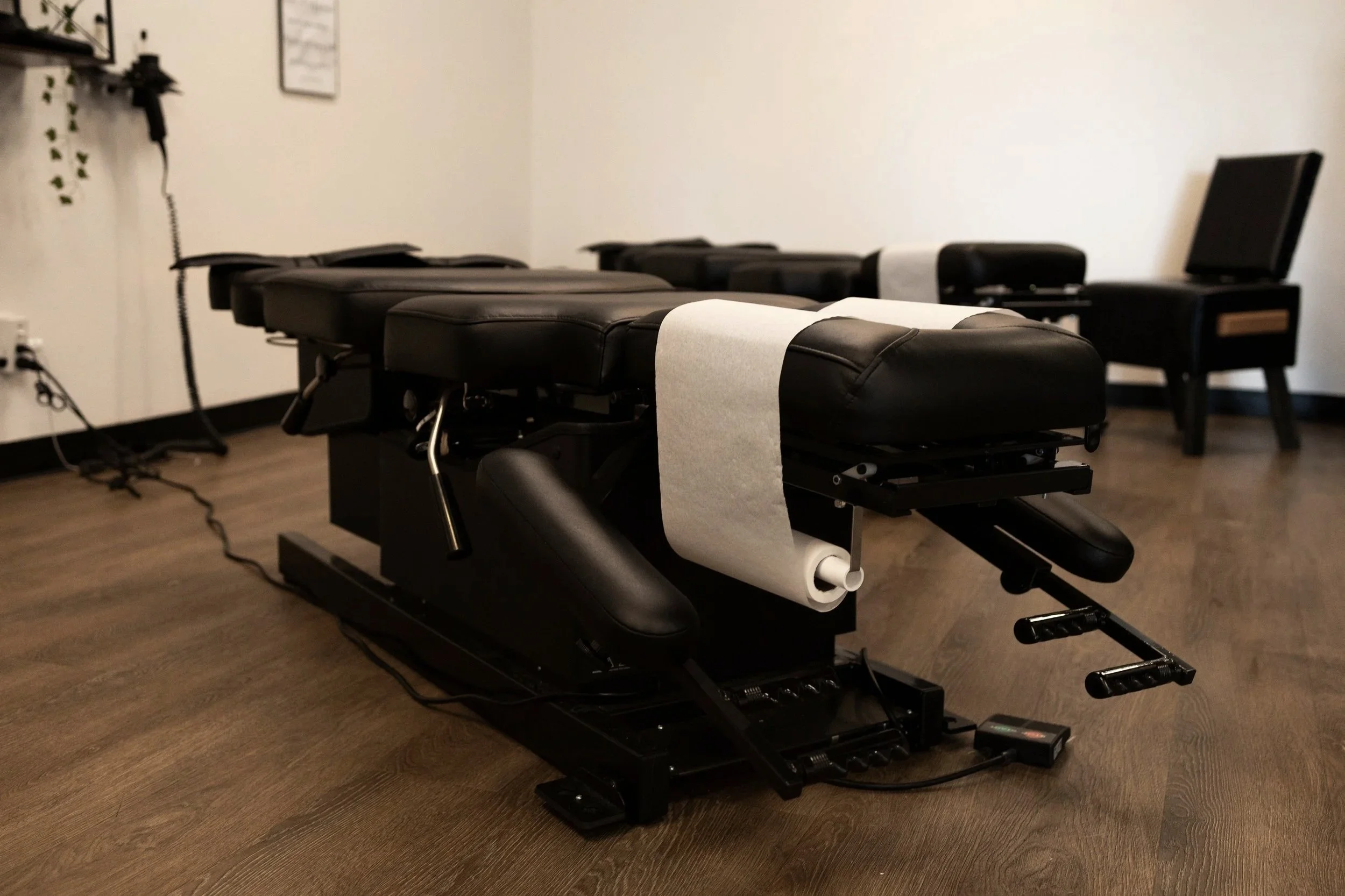 A chiropractic adjustment table in a clinic room, with a computer and an electronic device nearby.