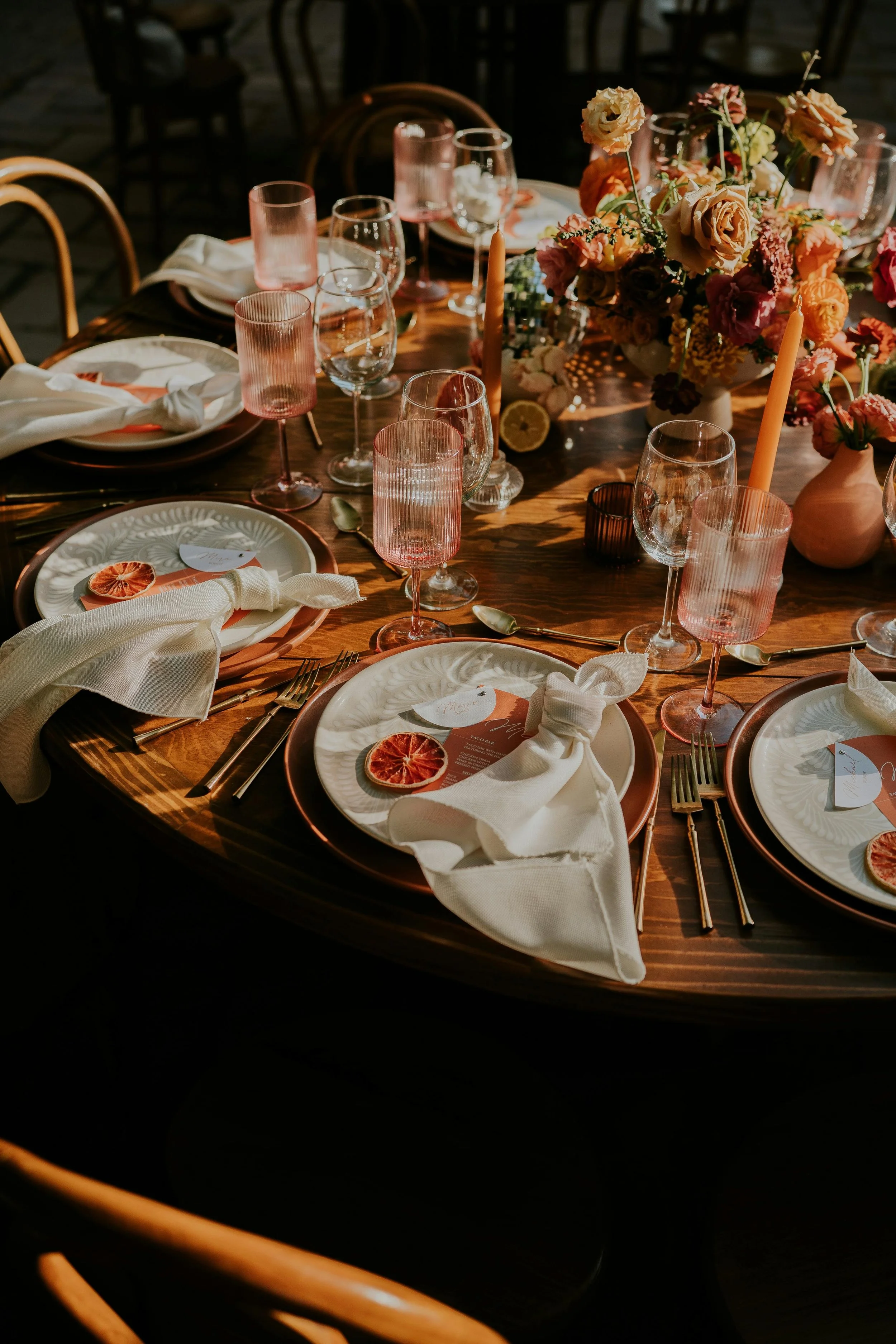 Carefully designed dinner table setting with citrus accents, warm candlelight, pink glassware, and floral arrangement — illustrating how environmental details shape the psychological state of guests in a relationship-driven experience.