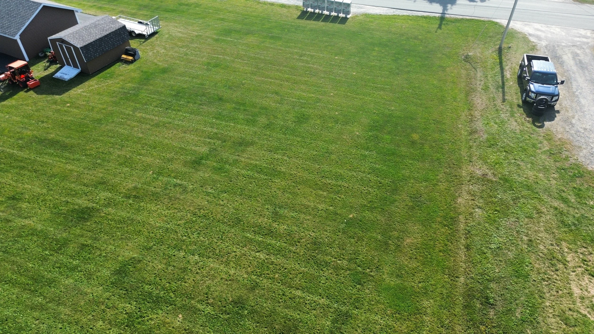 Aerial view of a large green grassy lawn with a small shed and a parked vehicle visible.