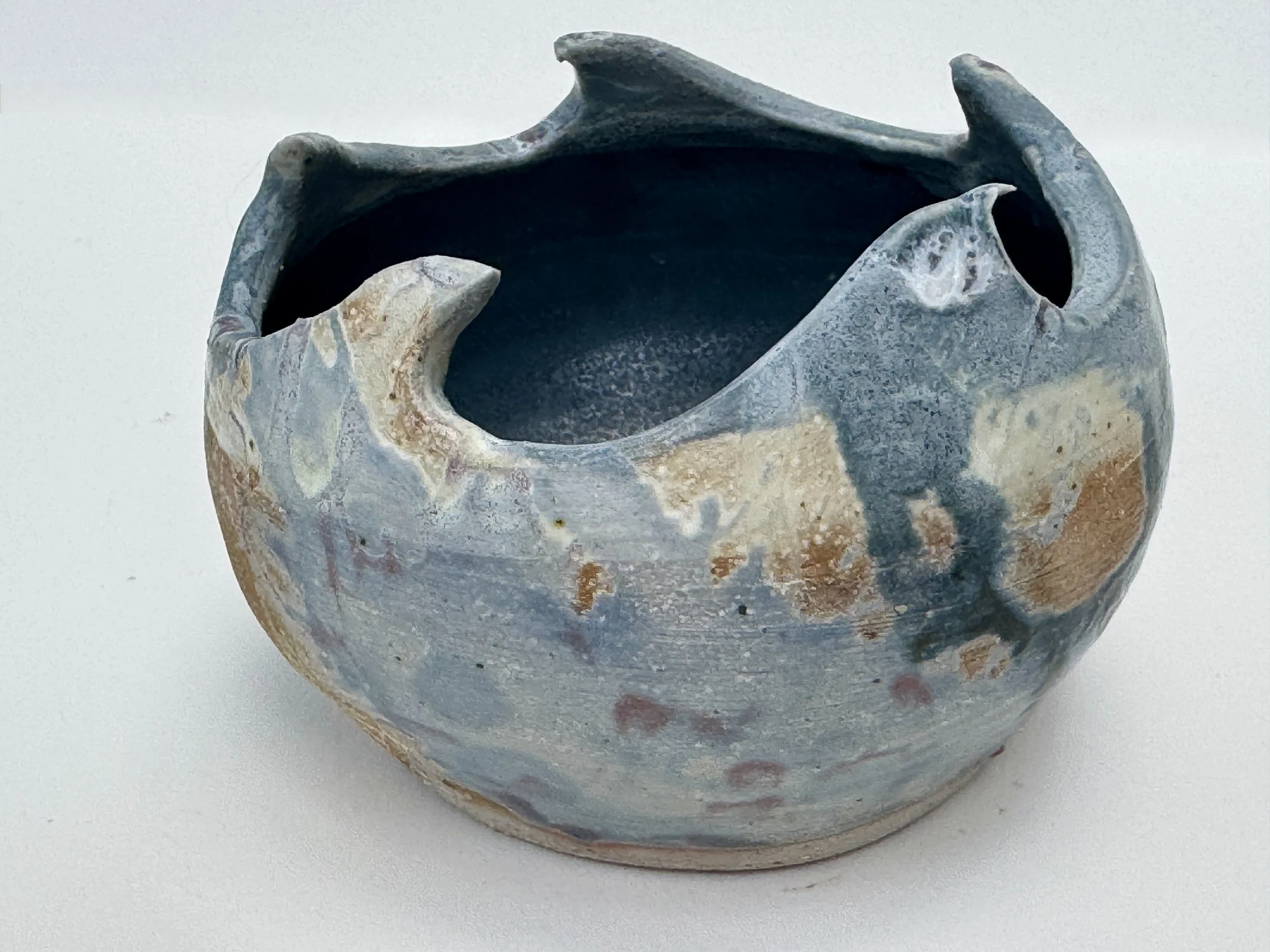 Wave shaped pot in blues, sandy beige and white depicting waves and the seashore. 15cms diameter, hand thrown and sculpted from white grogged clay.