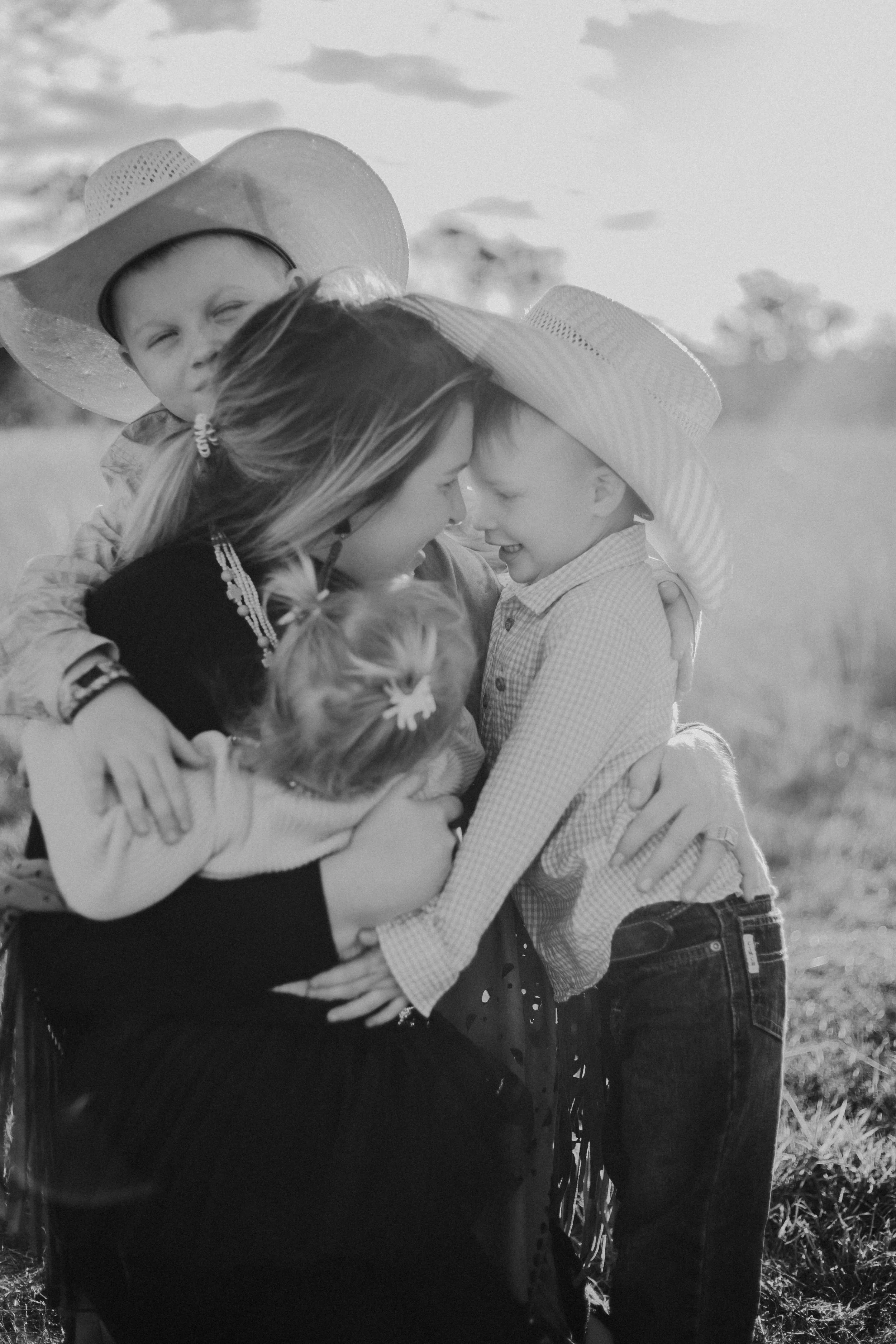 A family of five sharing a hug outdoors on a sunny day, all wearing hats.