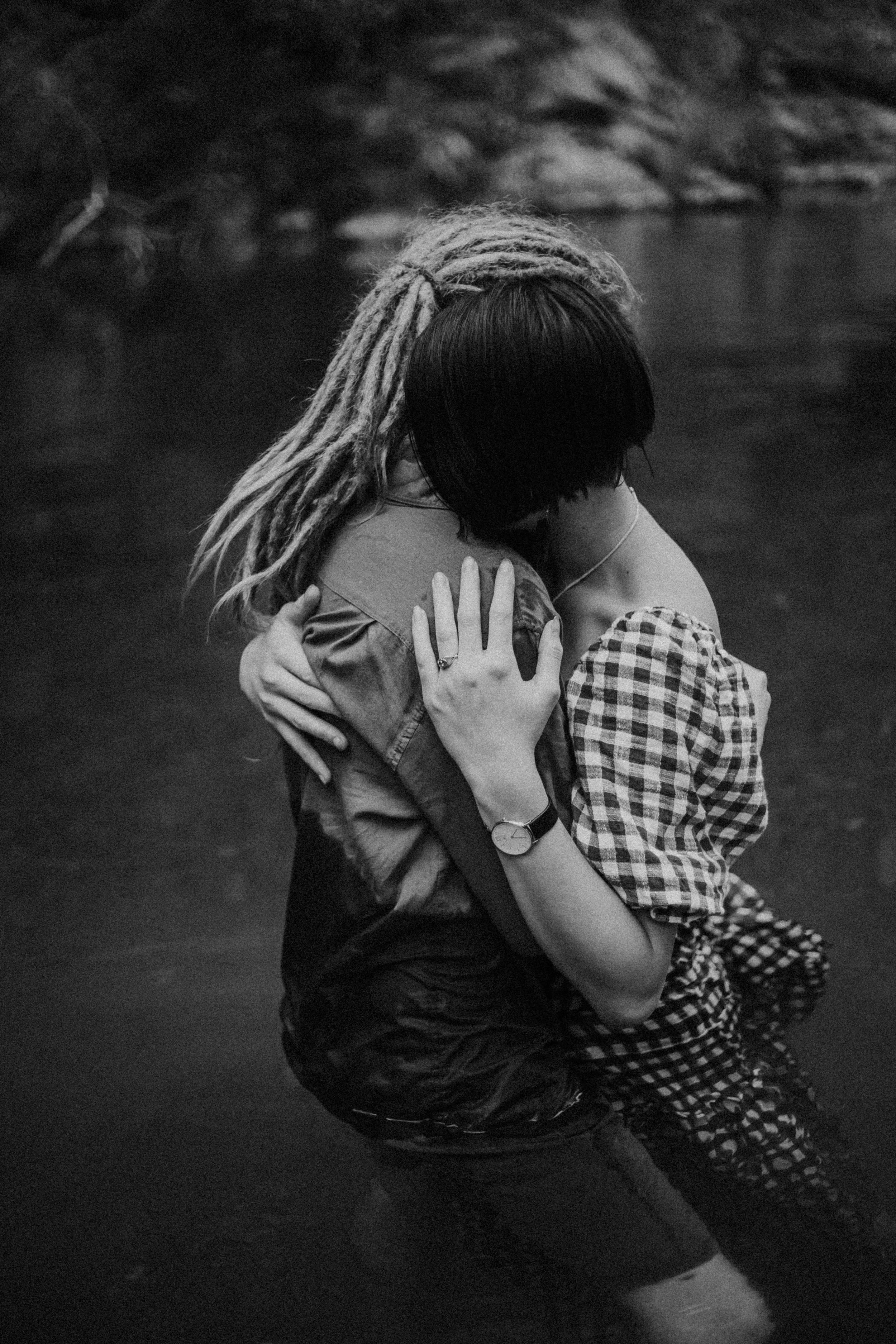 Two people embracing in a body of water, one has dreadlocks and the other has short dark hair and is wearing a checkered shirt.