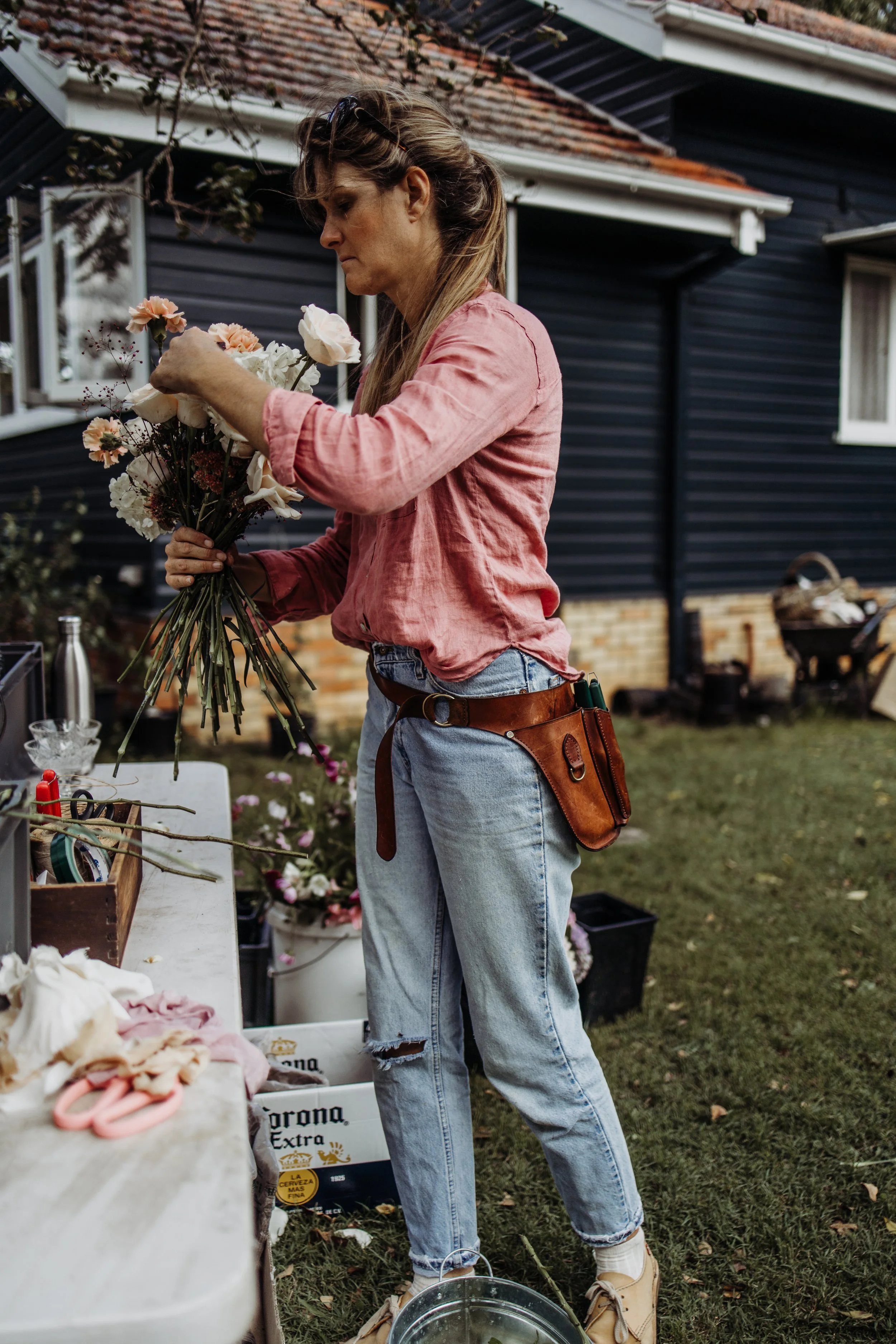 A woman arranging a bouquet of flowers outdoors near a table with crafting supplies.
