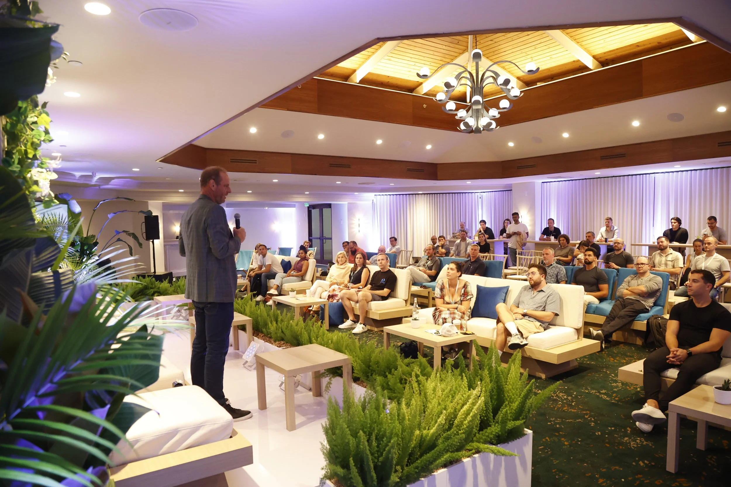 A panel of four speakers engaged in discussion on stage at the Arrington Founders Retreat, seated in modern chairs against a minimalist backdrop with soft lighting and greenery accents.