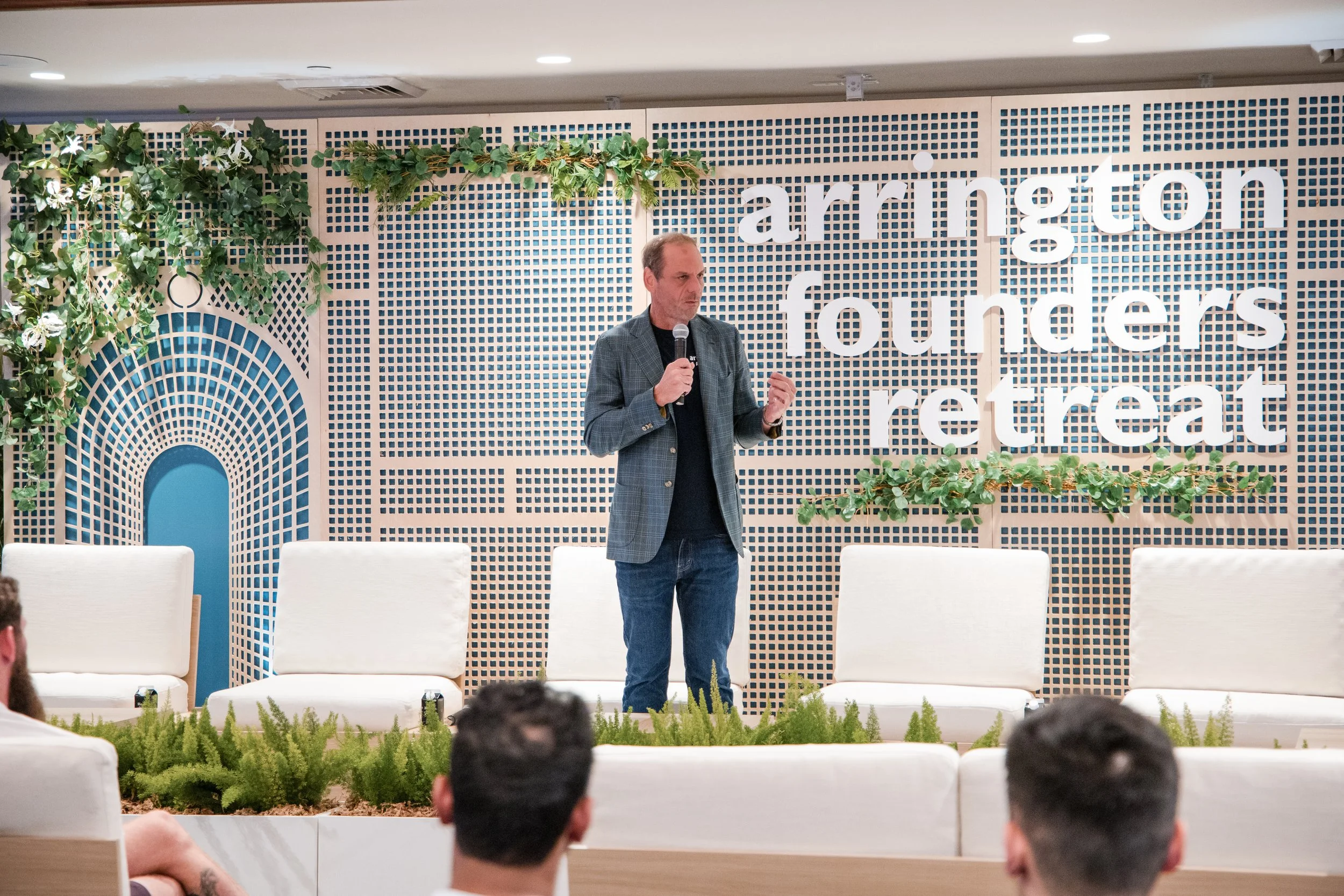 Michael Arrington speaking on stage at the Arrington Founders Retreat, addressing an audience in a relaxed, retreat-like setting with soft lighting and tropical Florida stage design.