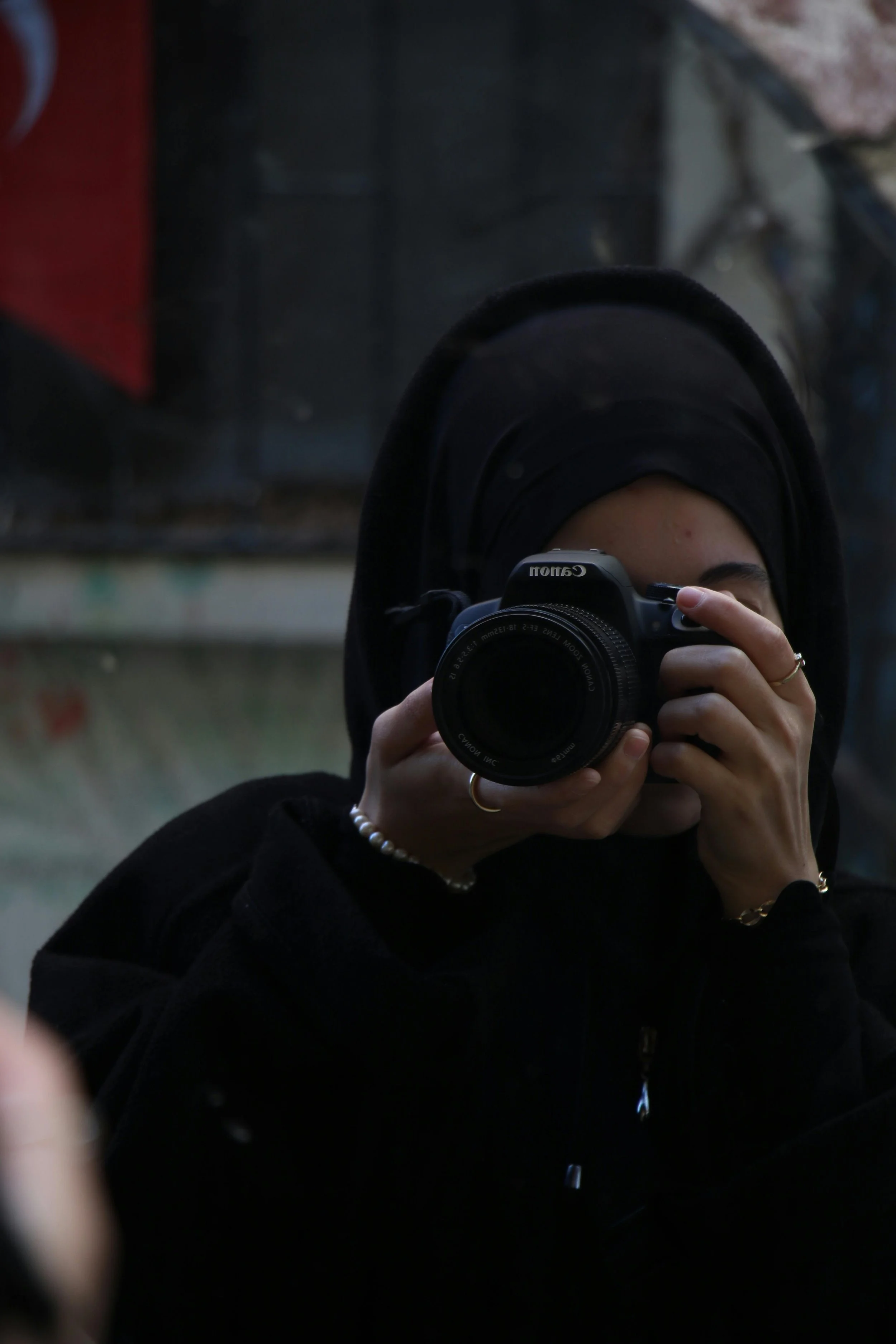 Person wearing a black hijab holding a DSLR camera close to their face, capturing a photo.