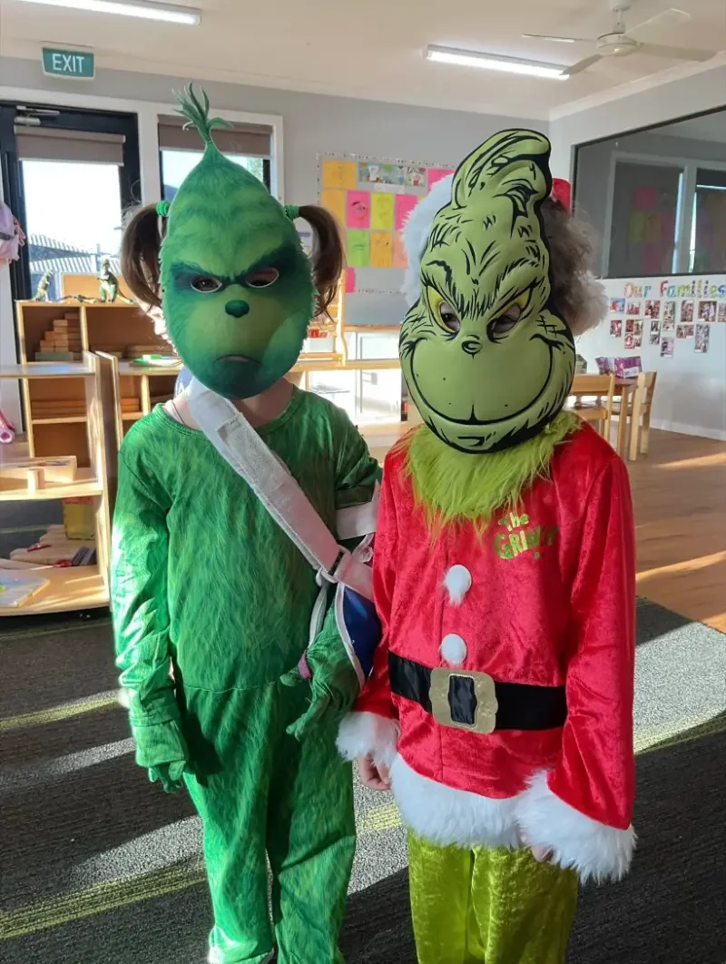 Two children dressed in Grinch costumes, standing in a classroom.