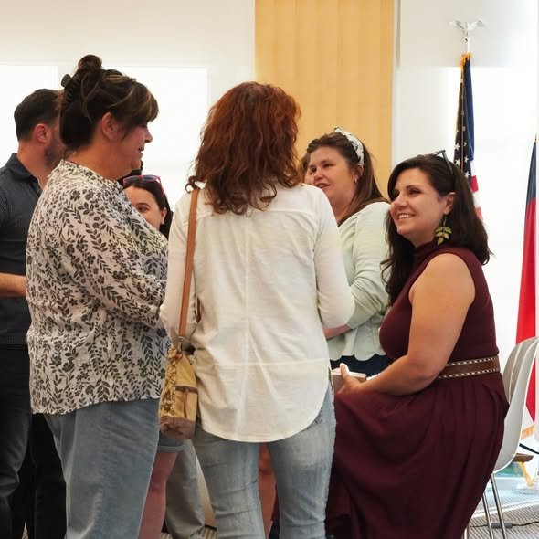 Group of women engaged in conversation at an indoor event, with US flag in the background.
