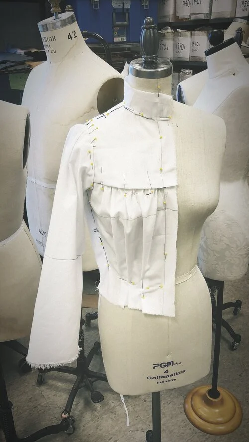Dress form with partially constructed garment, pinned fabric pieces to tailor a piece of clothing in a fashion design workspace.