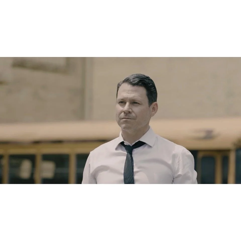 Man in white shirt and black tie looking serious outdoors.