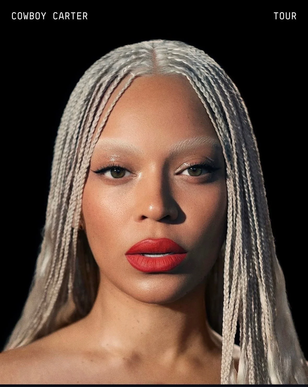 Close-up portrait of a woman with platinum blonde braids, bold red lipstick, and subtle eye makeup, against a black background.