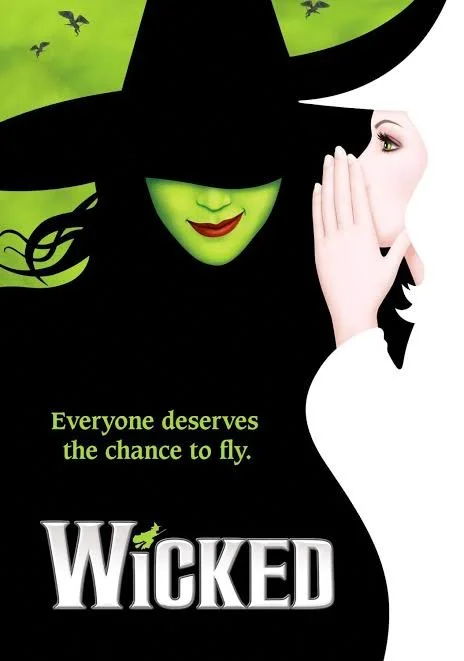A promotional poster for the musical Wicked featuring a green-faced witch with a pointed hat and a white-clad woman whispering.