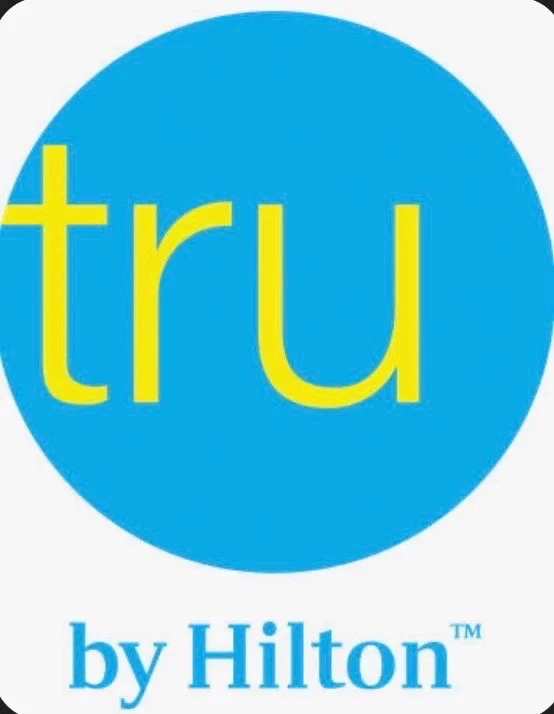 Logo of the 'tru by Hilton' brand, featuring a blue circle with the word 'tru' in yellow lowercase letters and 'by Hilton' below in blue.