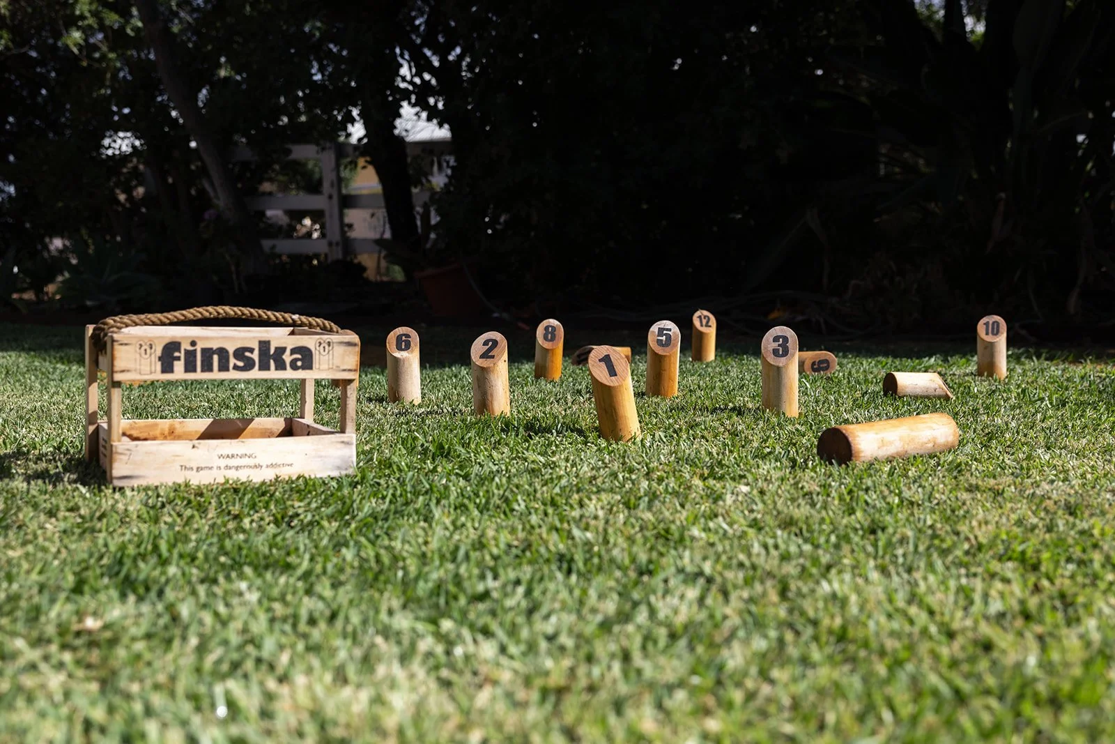 A wooden outdoor game setup on grass with a basket labeled 'finska' and numbered wooden logs arranged for a game.
