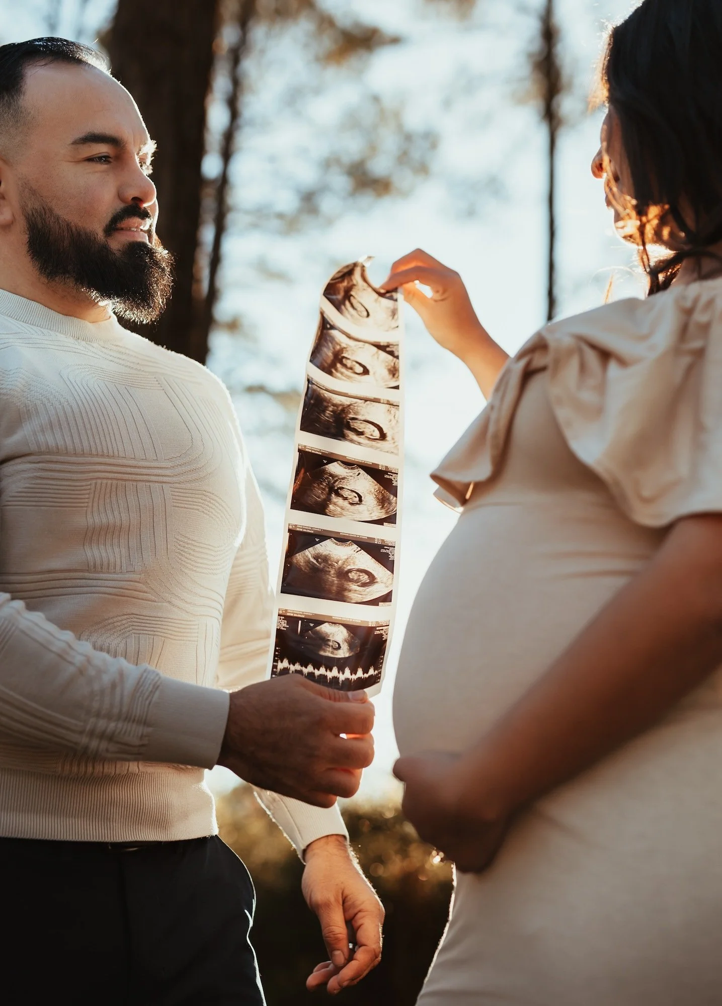 Man and pregnant woman outdoors looking at ultrasound images of their baby.