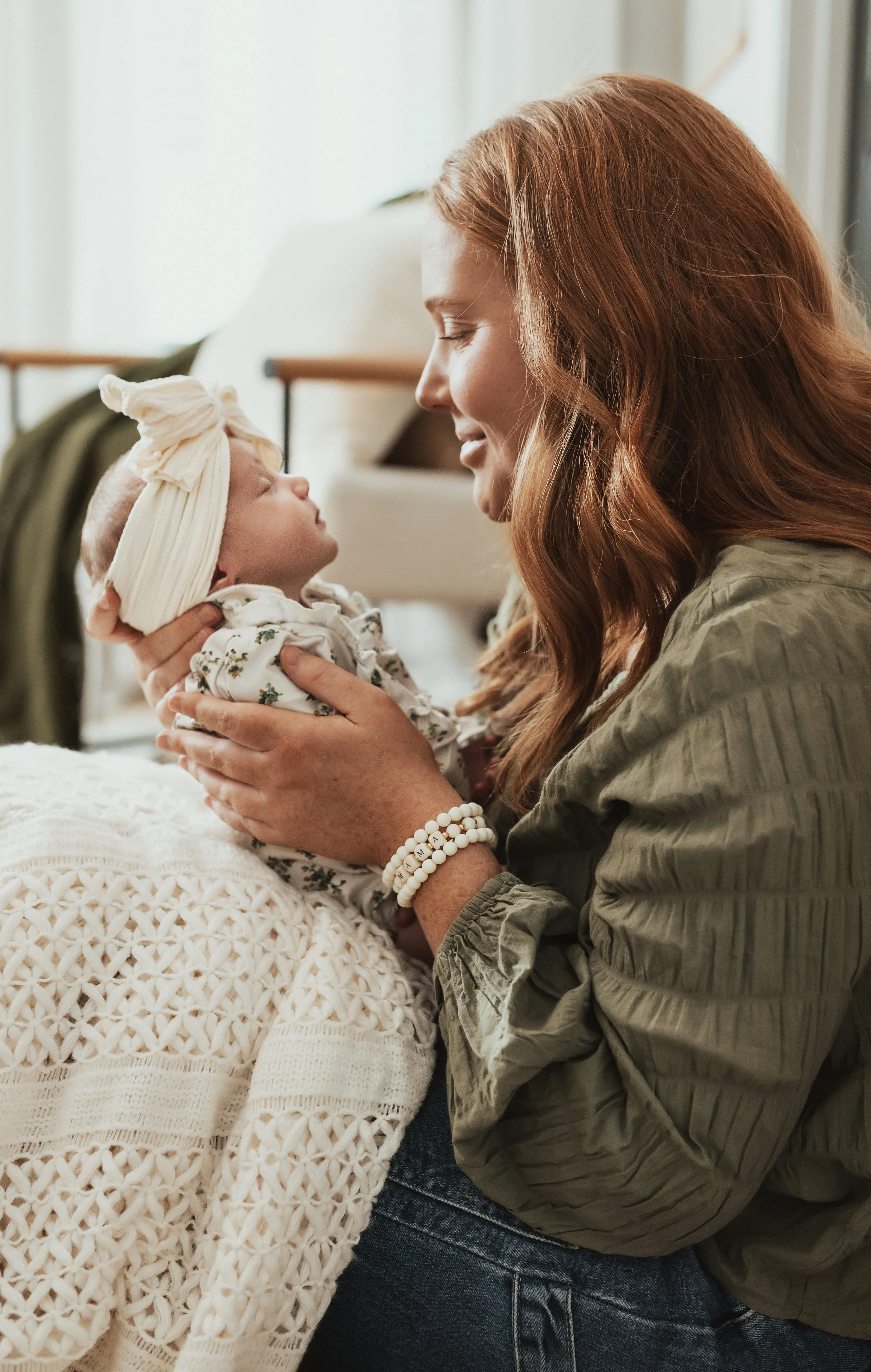 Woman holding a baby close, both smiling and making eye contact in a cozy indoor setting.