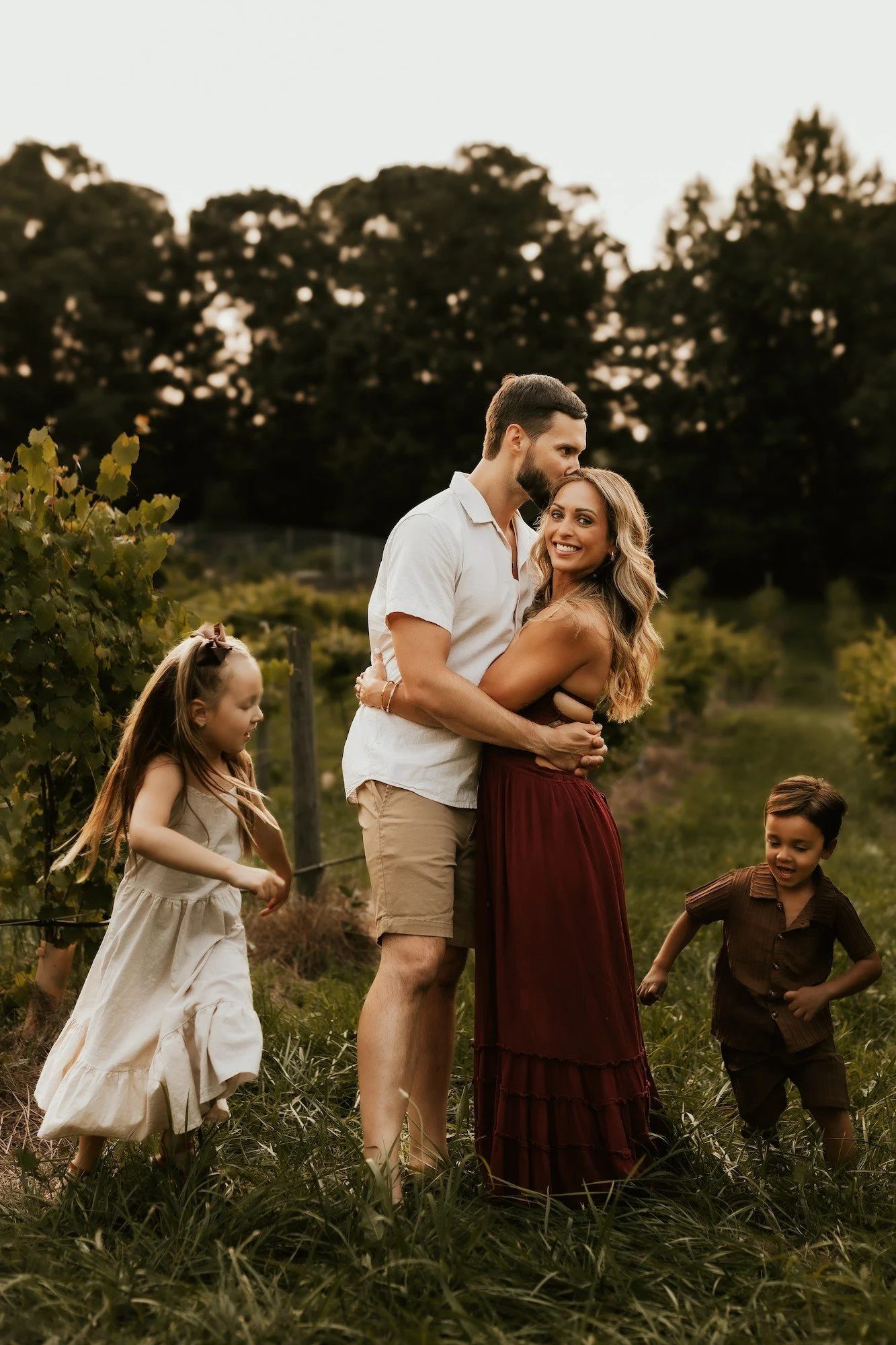 A happy family of four embracing outdoors in a field during sunset, with trees in the background.