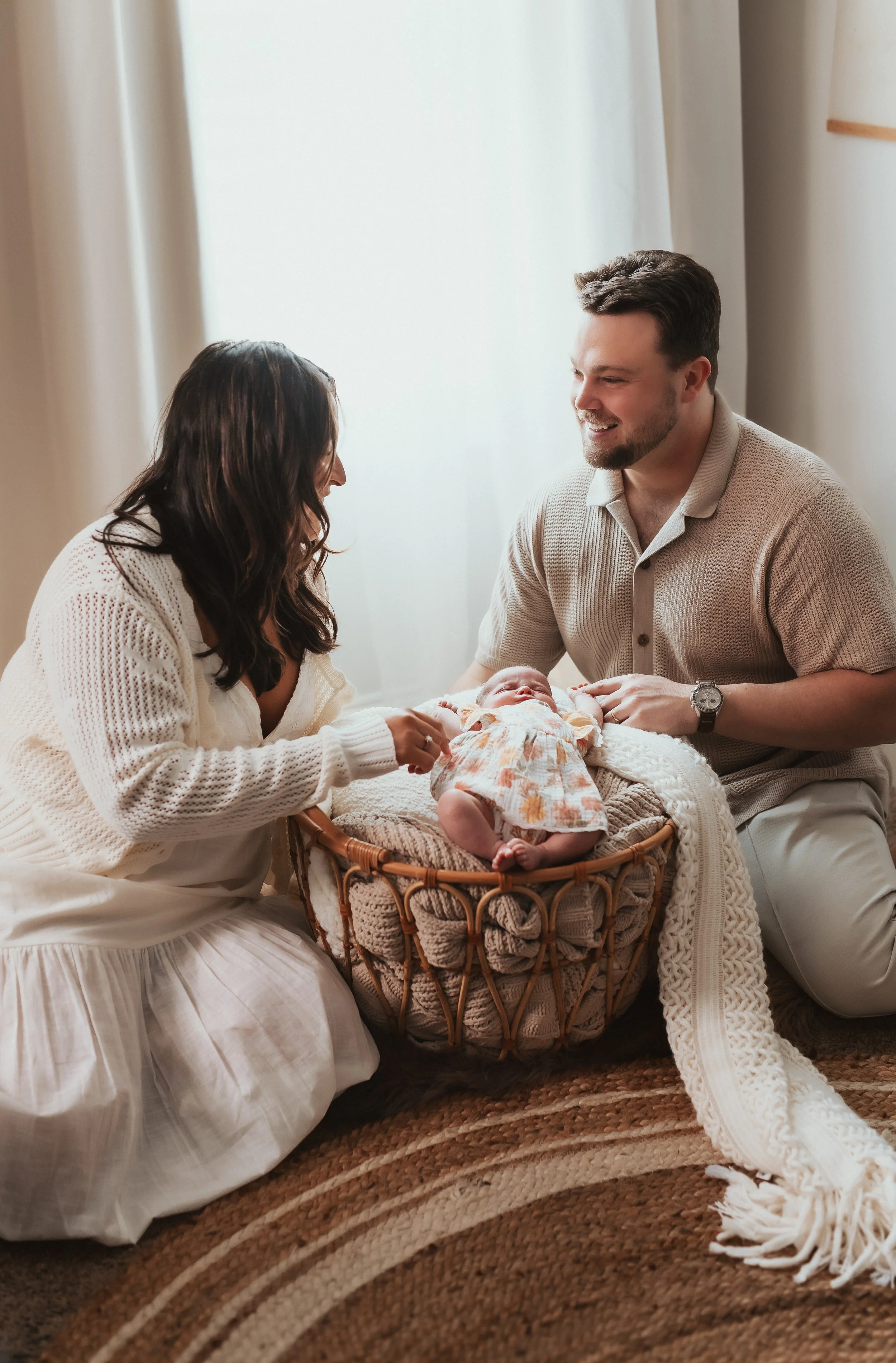 A family gathered around a bassinet with a newborn baby, sharing a tender moment in soft natural light.