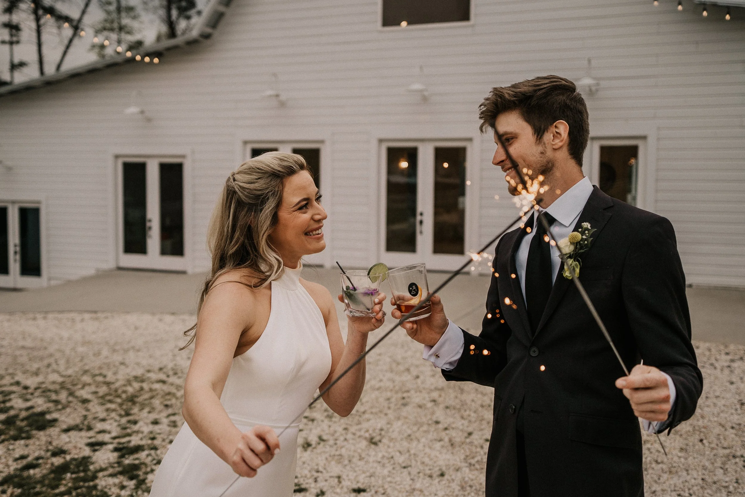 bride and groom with sparklers in front of white wedding venue; how do we get our wedding guests to RSVP?
