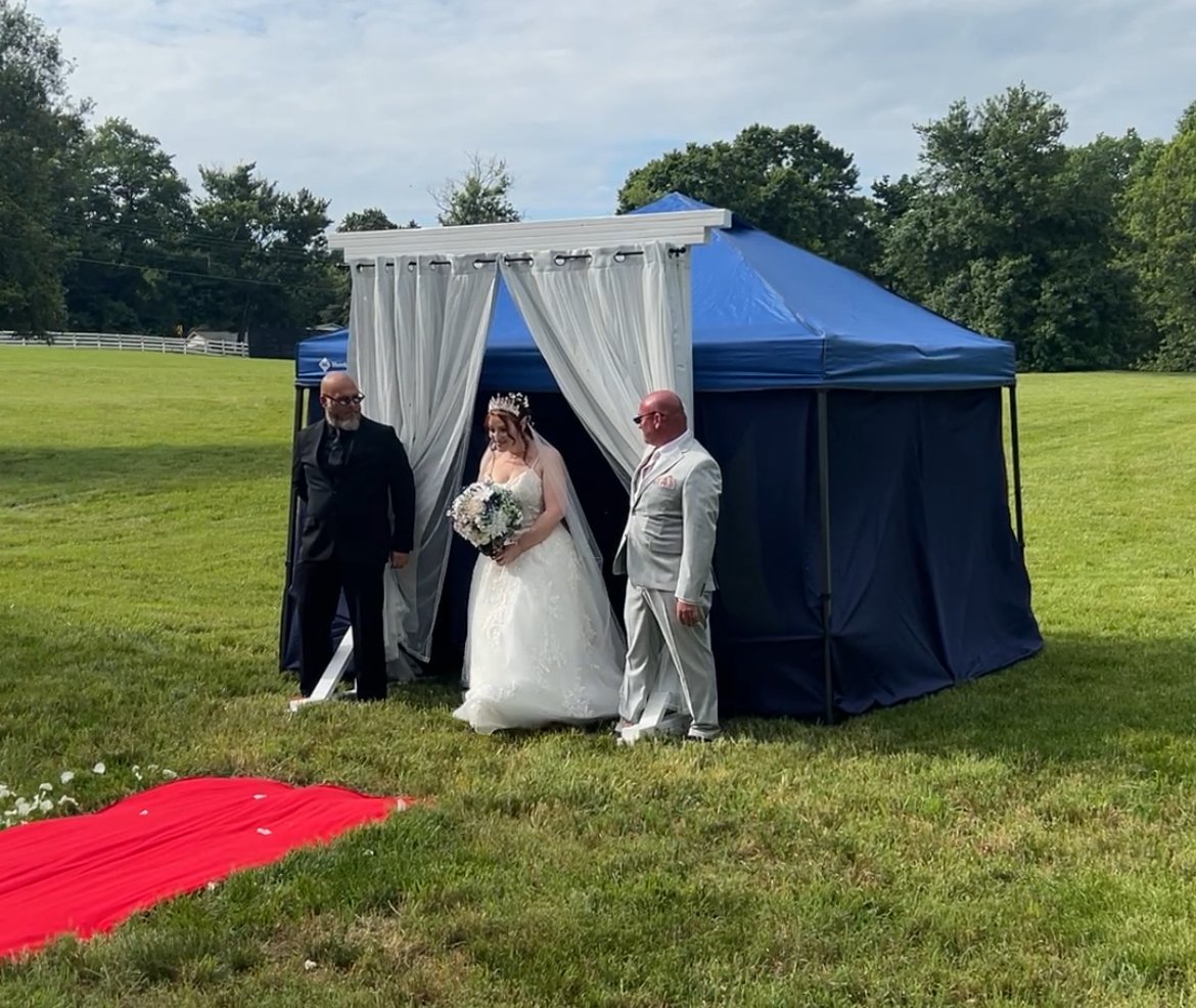 Bride and fathers walking through a doorway with curtain in a meadow