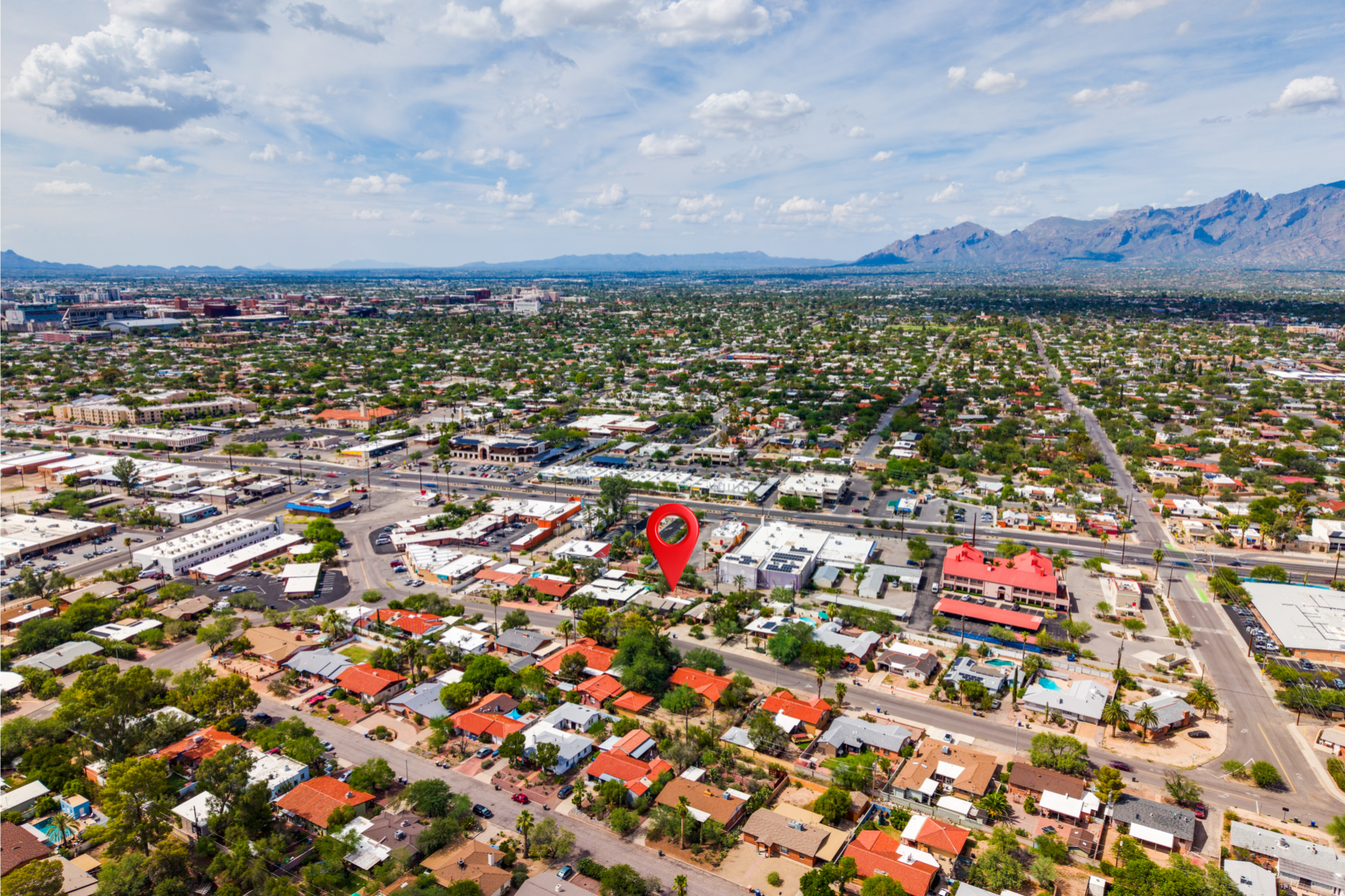 Aerial view of a city with buildings, streets, and houses, with mountains in the background, under a partly cloudy sky.