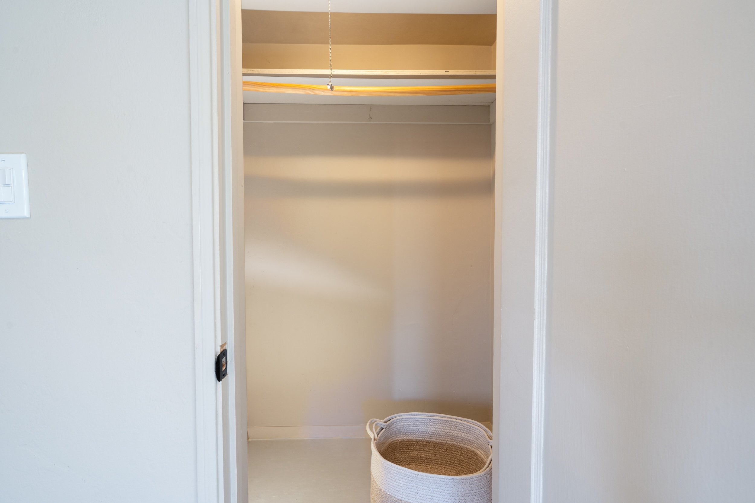 Empty closet with beige shelving and a neutral wall, with a beige woven basket on the floor in front.