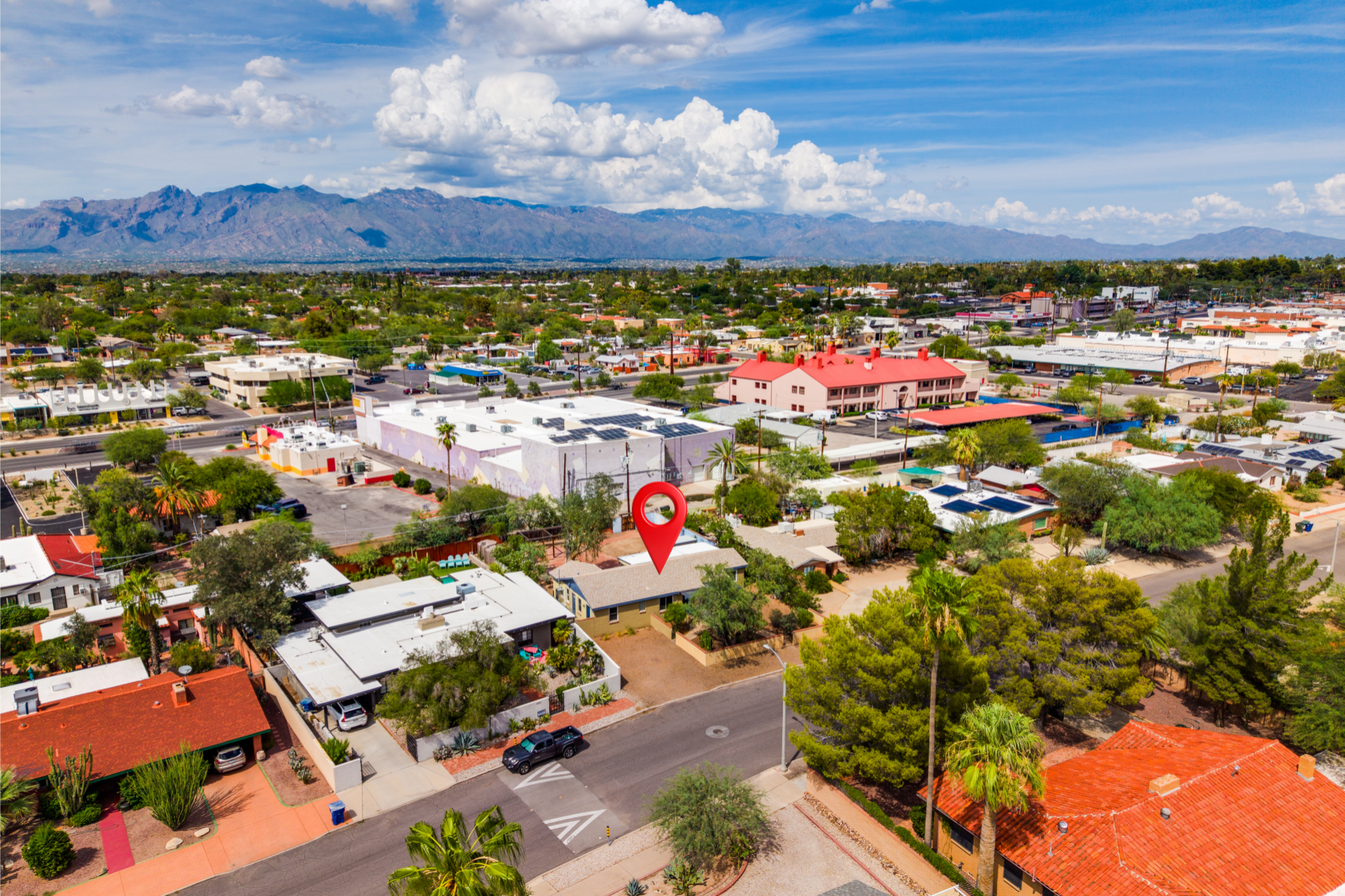 Aerial view of a suburban neighborhood with houses, trees, and streets, with mountains in the background under a partly cloudy sky.